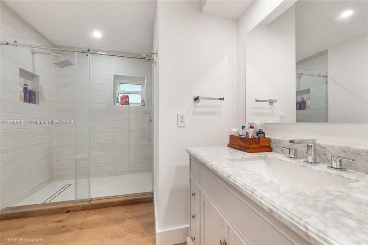 A bathroom with a vanity, a mirror, and a shower room.