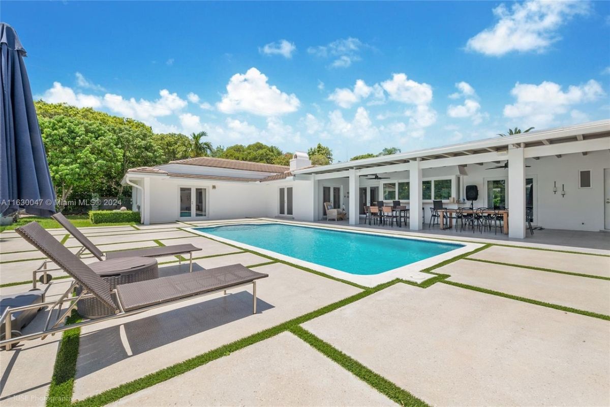 A swimming pool with an umbrella and comfy chairs.