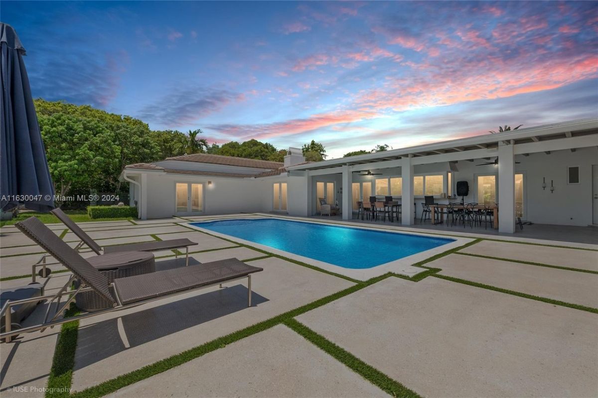 A swimming pool with an umbrella and comfy chairs.