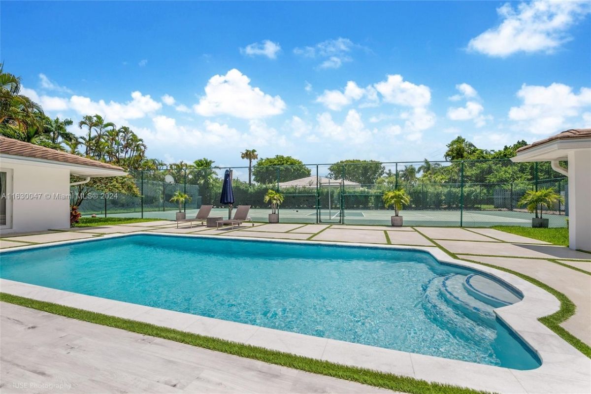 A swimming pool with an umbrella and comfy chairs.