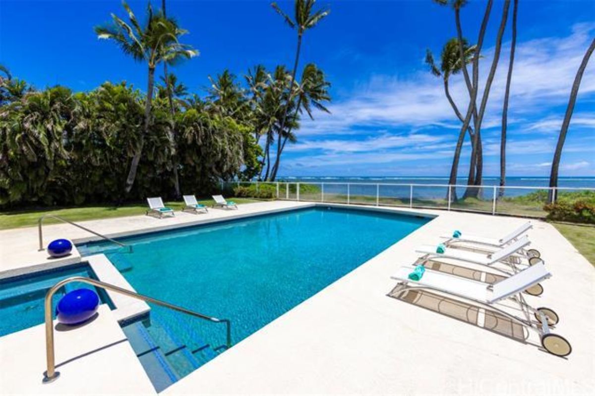 A swimming pool with a jacuzzi, comfy chairs, and trees.