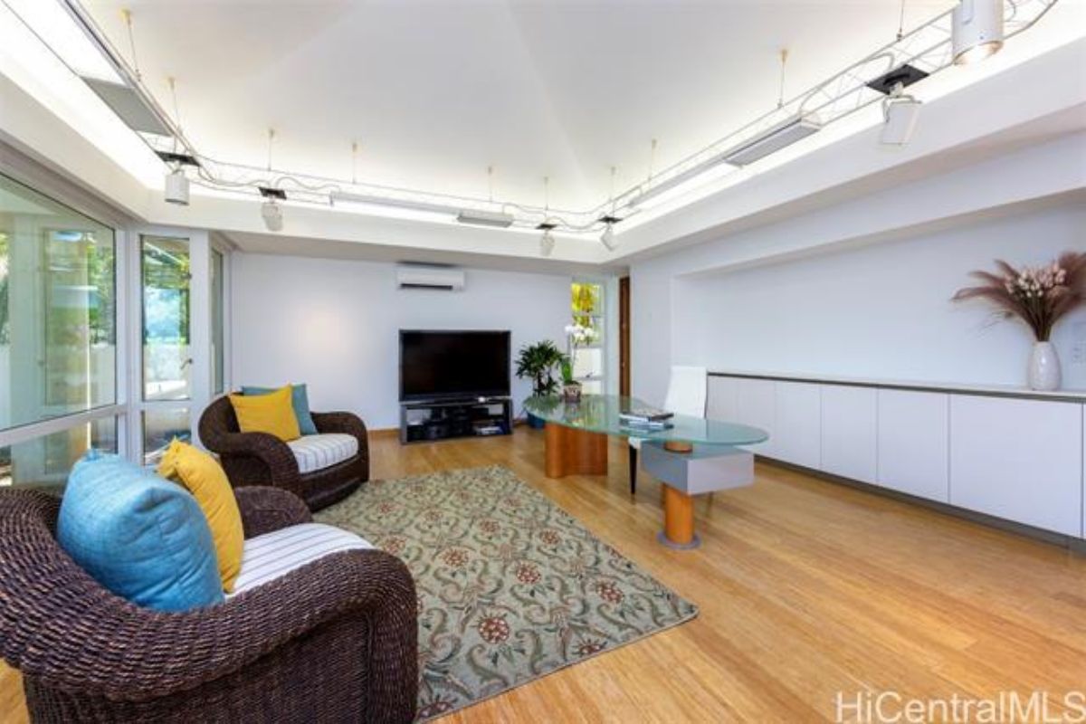 A home office with a window, TV, chairs, rug, and a desk with an office chair.