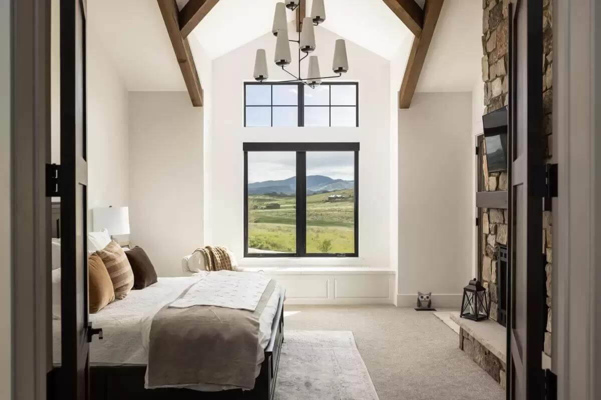 Primary bedroom with a dark wood bed, a vaulted ceiling, and black-framed windows.