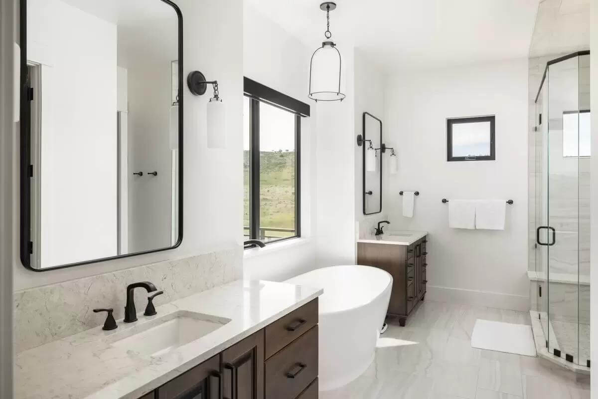 Primary bathroom with a glass-enclosed shower, and his and her vanities flanking the soaking tub.