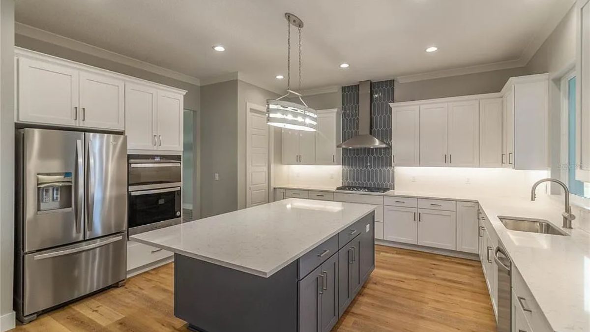 A kitchen with a center island, cabinets, countertop, sink, and kitchen appliances.