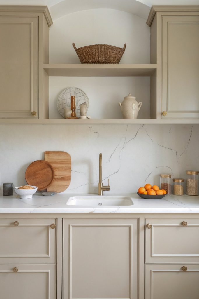 A beige kitchen with marble countertops, brass faucet, open shelves, and minimalist decor.