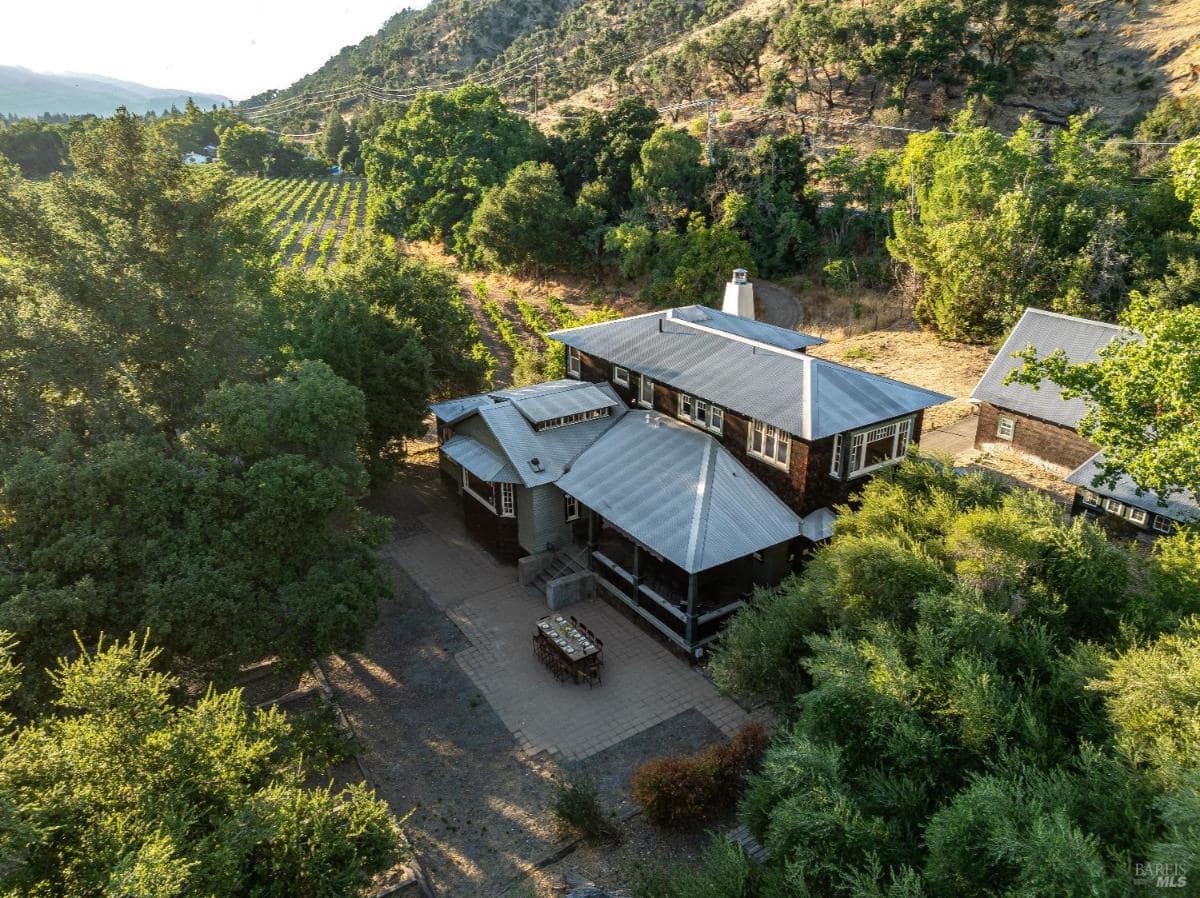 Aerial view of a house surrounded by trees, vineyards, and hills.