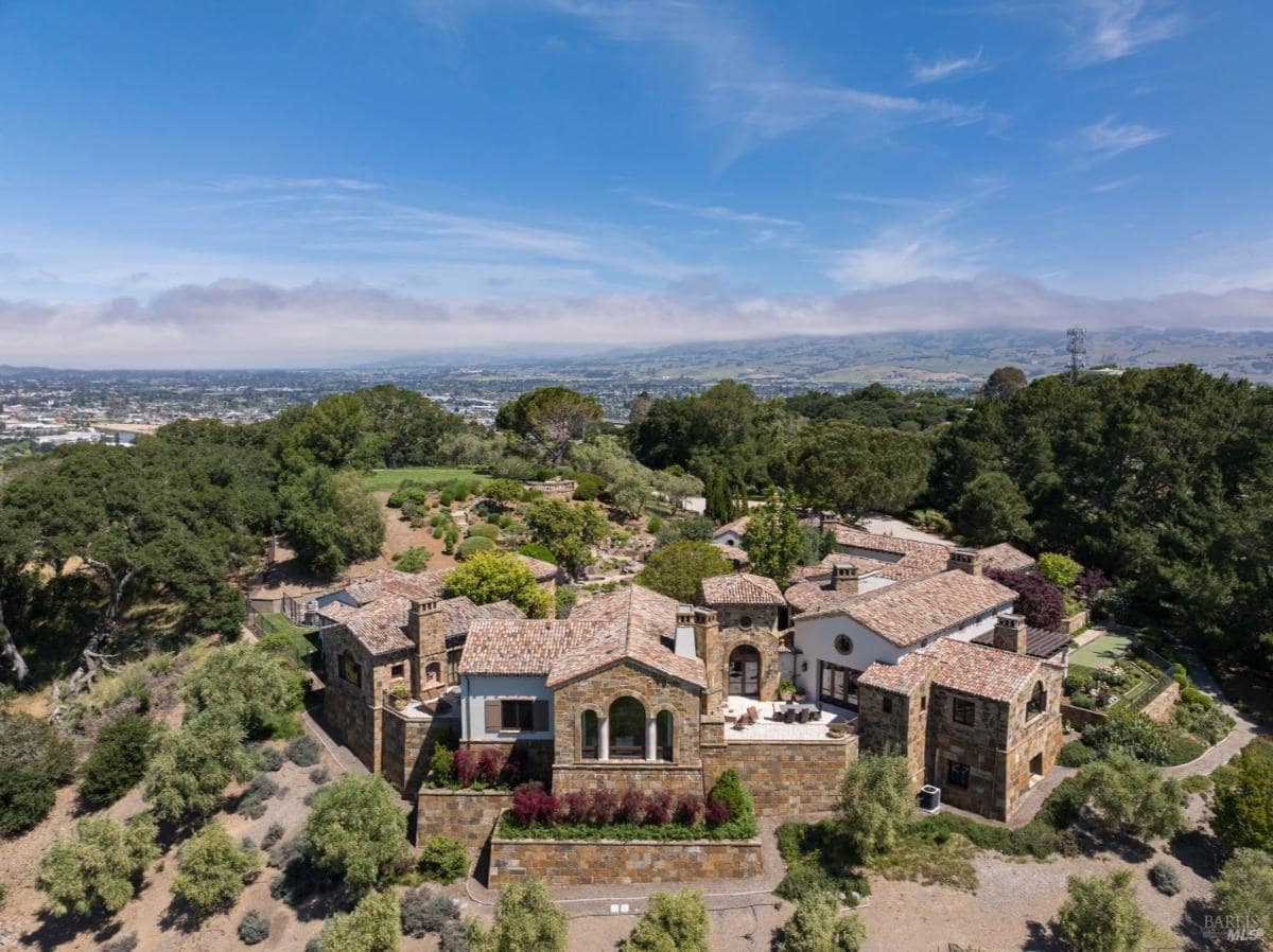 An aerial view of a large stone home on a hill surrounded by greenery.