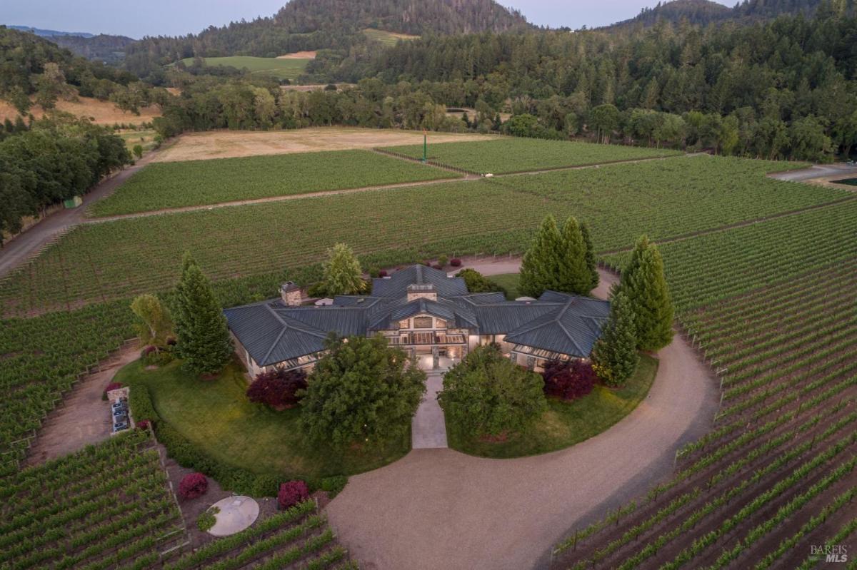 Aerial view of a large house located in a vineyard surrounded by fields and trees.