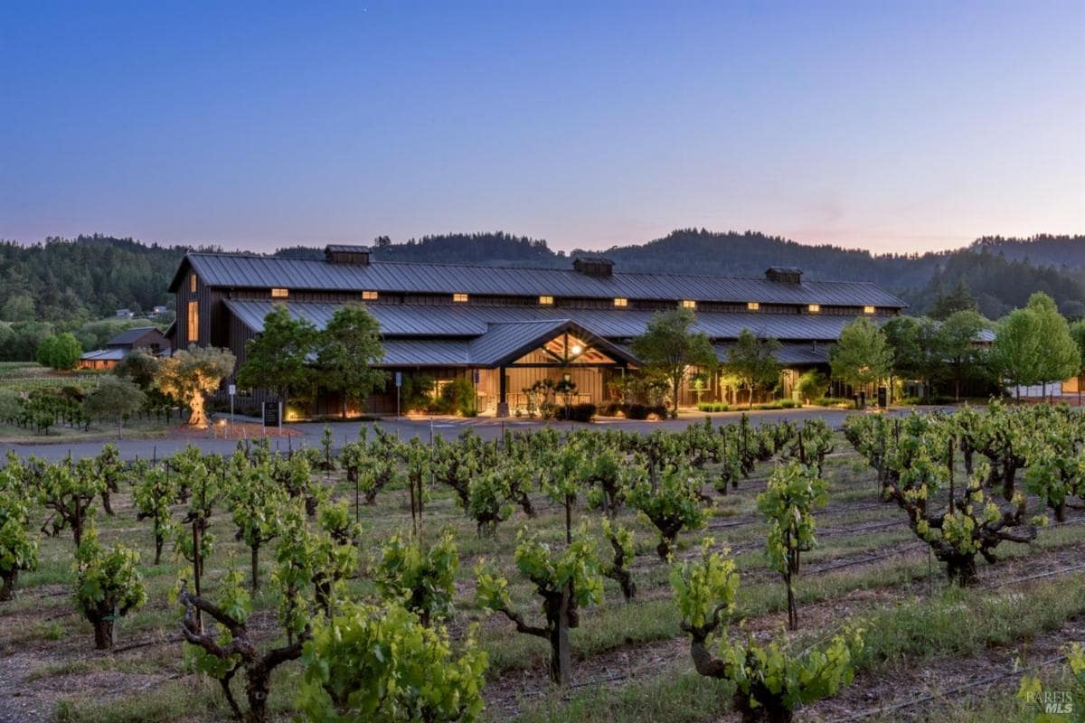 Exterior view of a large building surrounded by a vineyard at dusk.