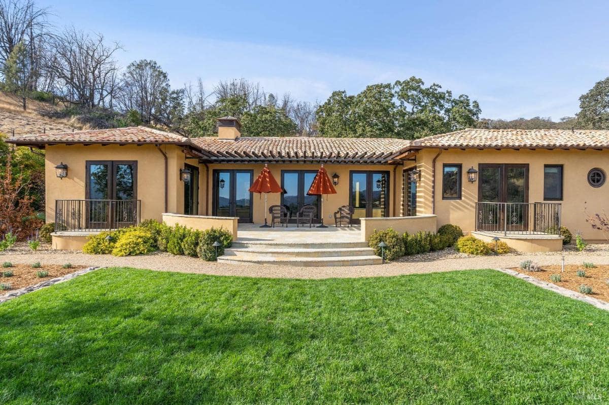 Front view of a single-story house with a patio and steps leading to a lawn.