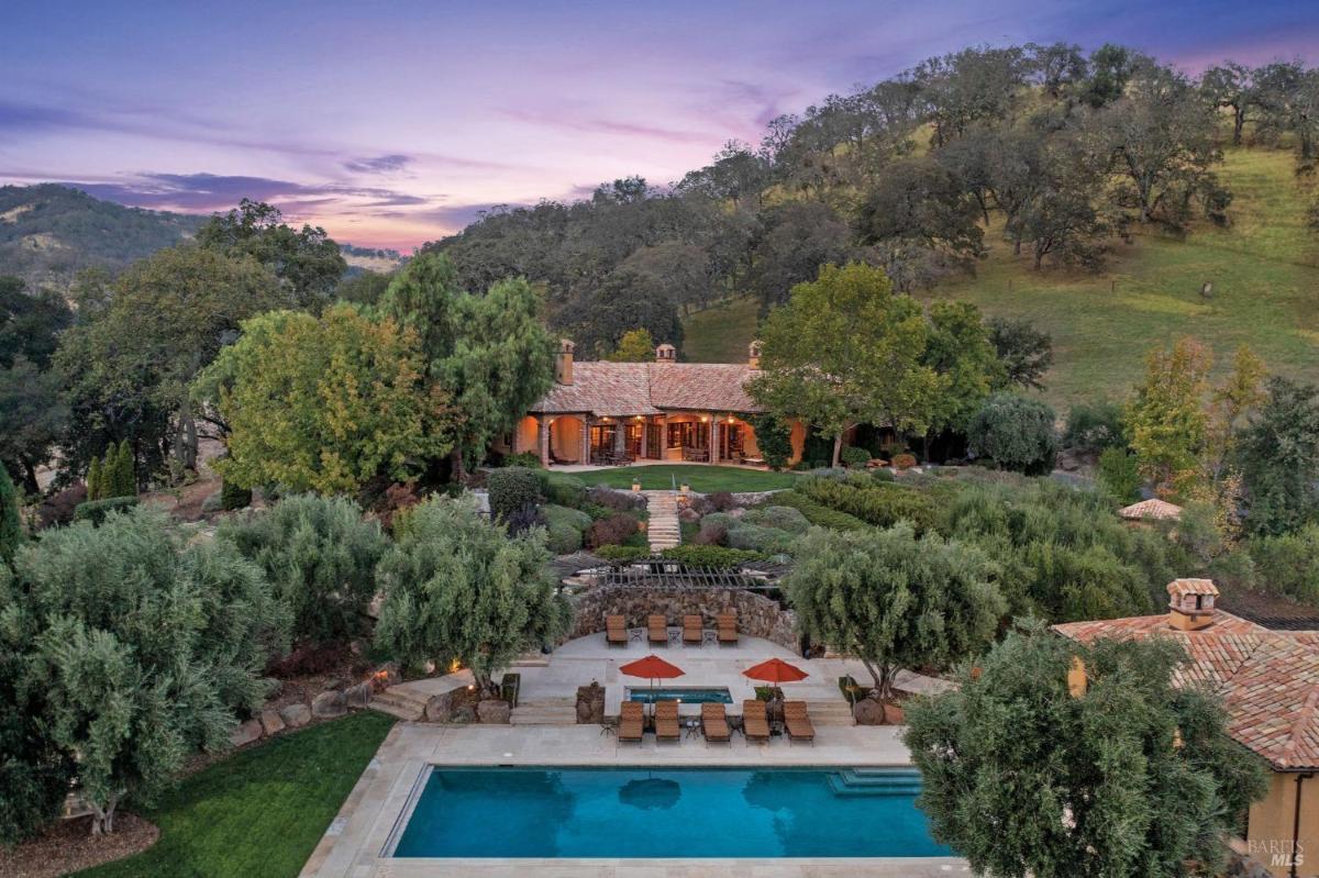 Aerial view of a house with a swimming pool, surrounded by trees and hills.