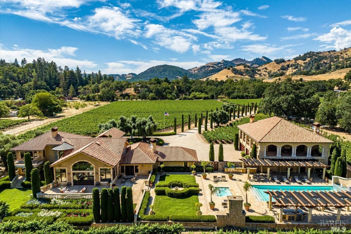 Aerial view of a mansion with a vineyard in the background.