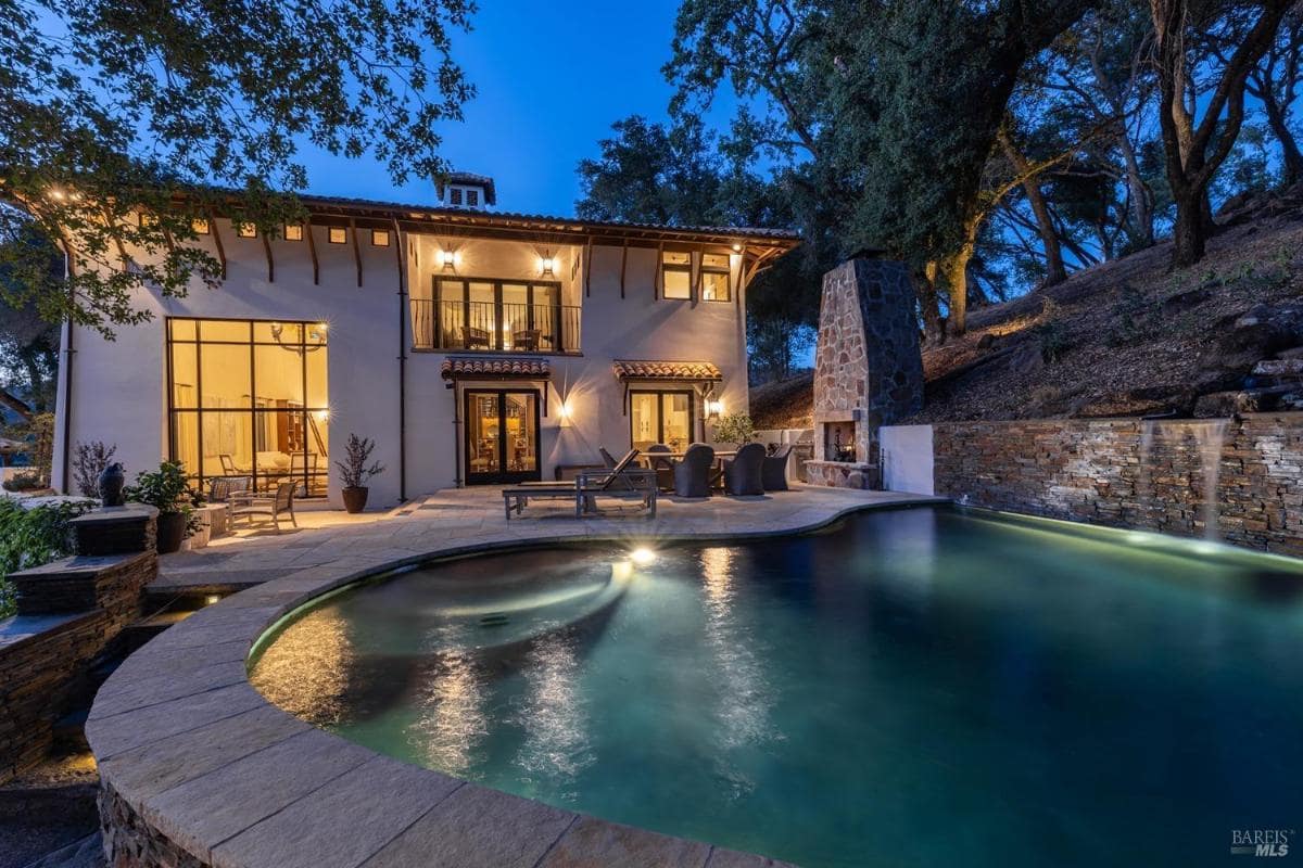 A two-story house with a pool, outdoor seating area, and a stone fireplace.