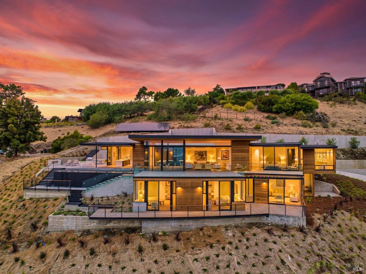 A modern, multi-level home with large glass walls on a hillside.