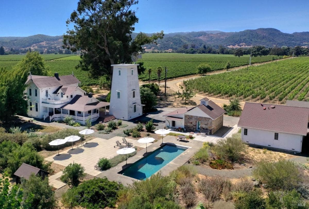 An aerial view of a mansion featuring a swimming pool, main residence, surrounding greenery, and nearby hills