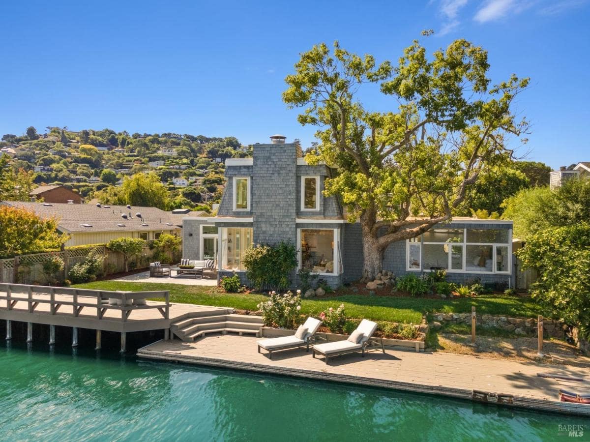 A waterfront home with a wooden deck and outdoor seating overlooking the water.