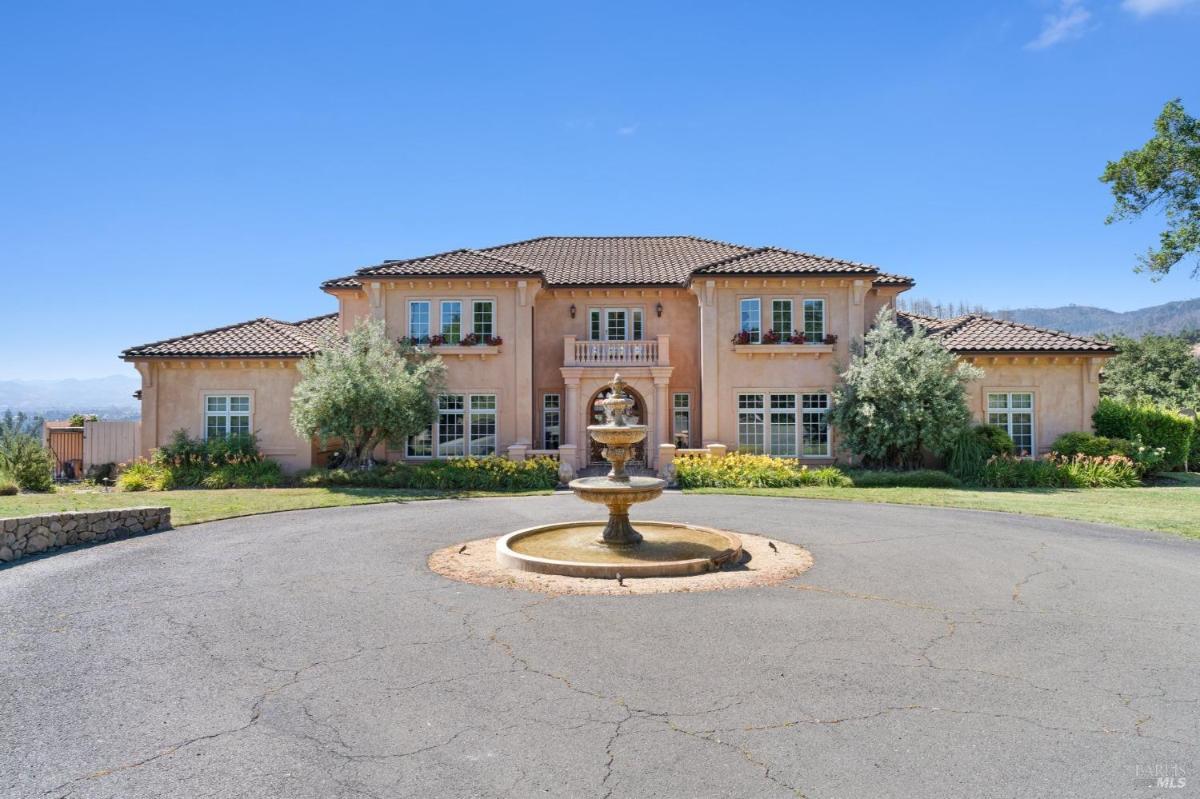 Mediterranean-style home with a central fountain, circular driveway, and mountain views.