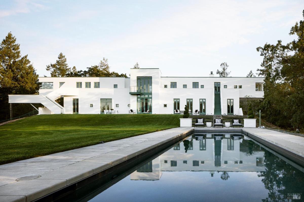 Large white modern mansion with a reflective pool and expansive lawn.