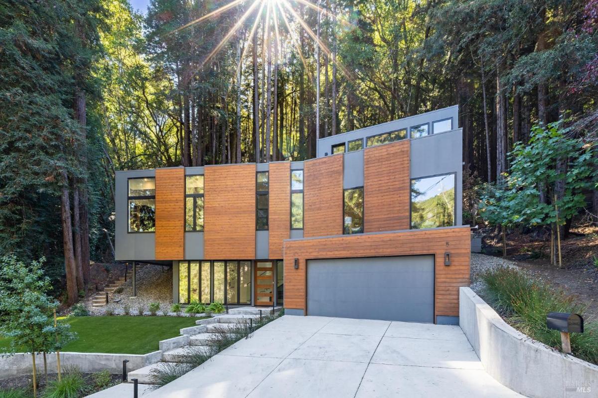 Modern home exterior with wood and glass paneling surrounded by trees.