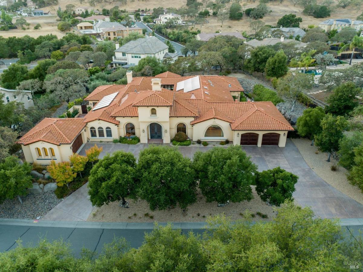 A large house with a red tile roof, surrounded by trees and a driveway.