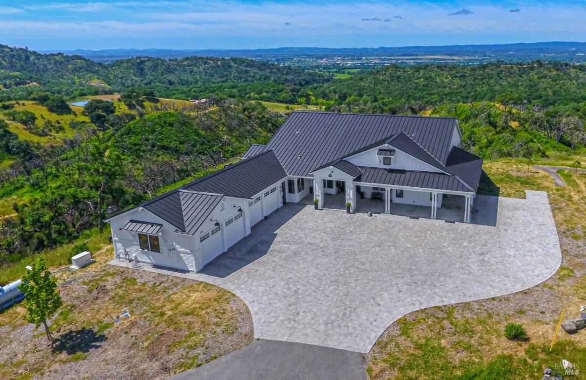 Aerial view of a house with a large driveway surrounded by hills and greenery.