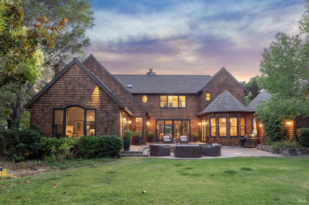 Rear view of a house with wood siding, outdoor seating, and lawn.