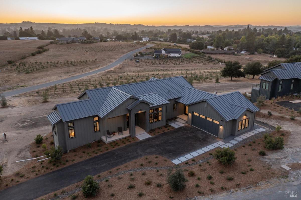 An aerial view of a modern house with a driveway and surrounding landscape at dusk.