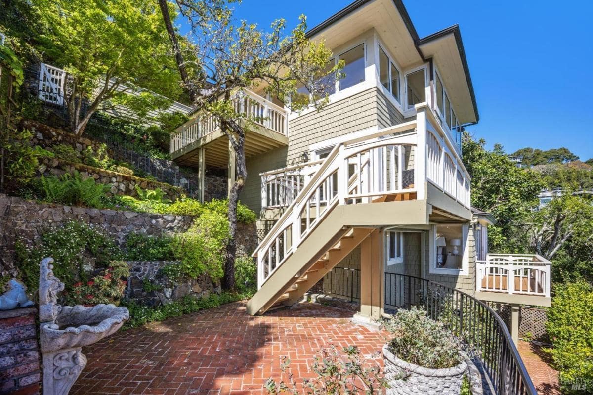 A multi-level house with a stone patio, brick steps, and surrounded by greenery.