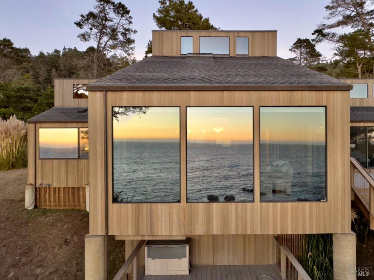 House exterior with large windows reflecting ocean view.