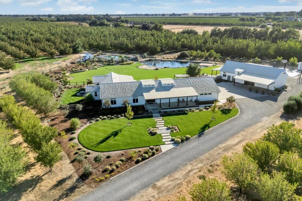 An aerial view of a property with landscaped gardens, a pond, and multiple structures.