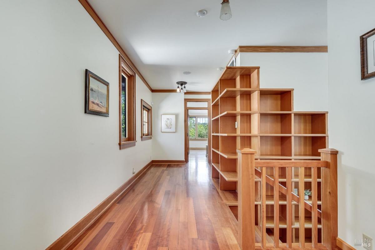 Hallway with wooden flooring, built-in shelves, and windows.