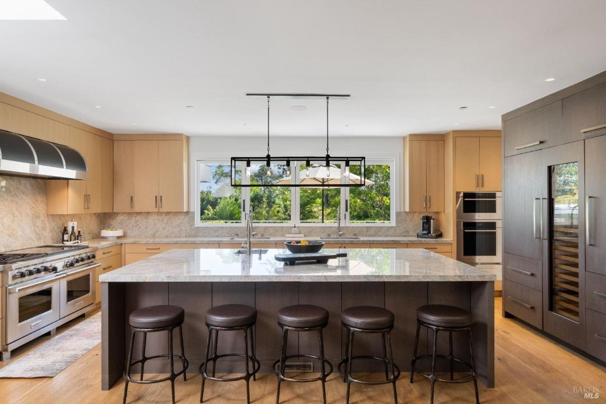 A kitchen with a central island, a range, built-in appliances, and windows overlooking trees.