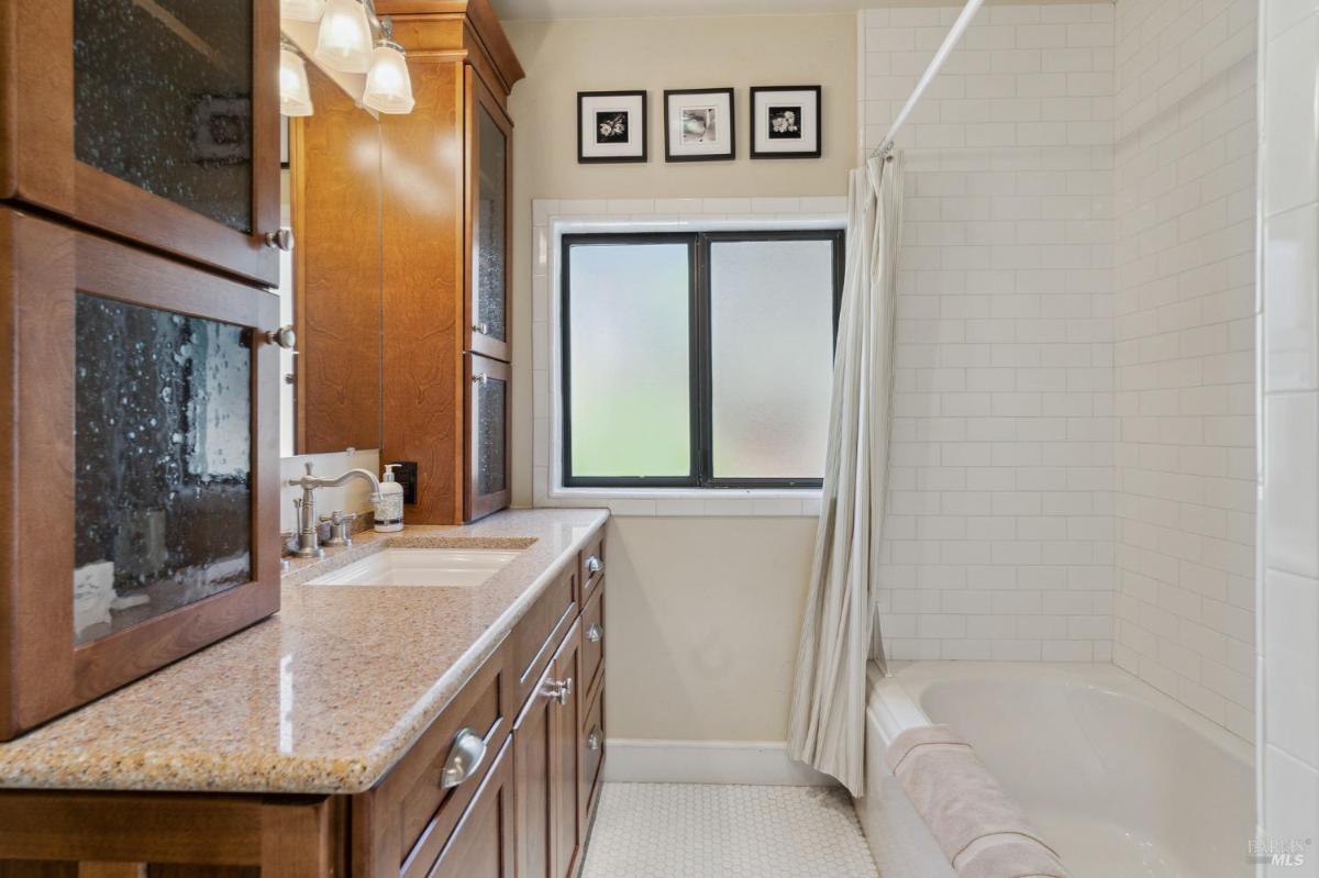 A bathroom with a shower-tub combo and a wood vanity with a mirror.