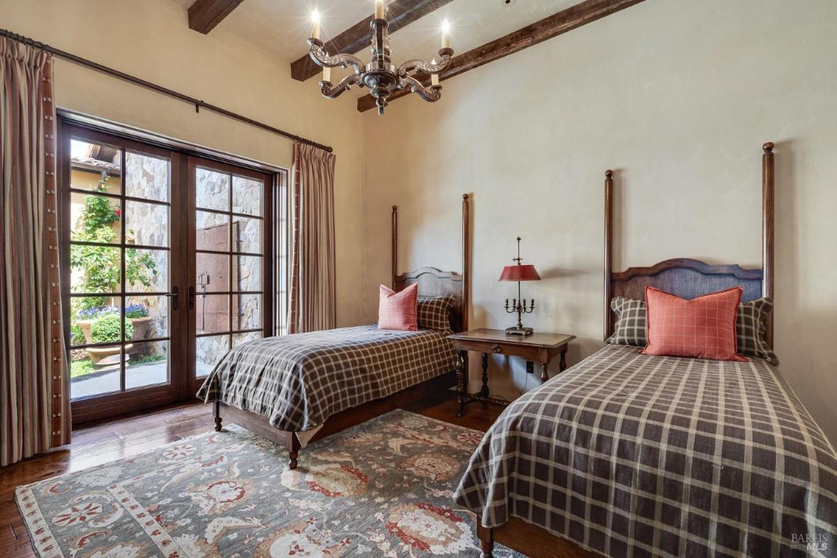 Bedroom with two twin beds, wooden frames, plaid bedding, a small side table, and French doors leading outside.