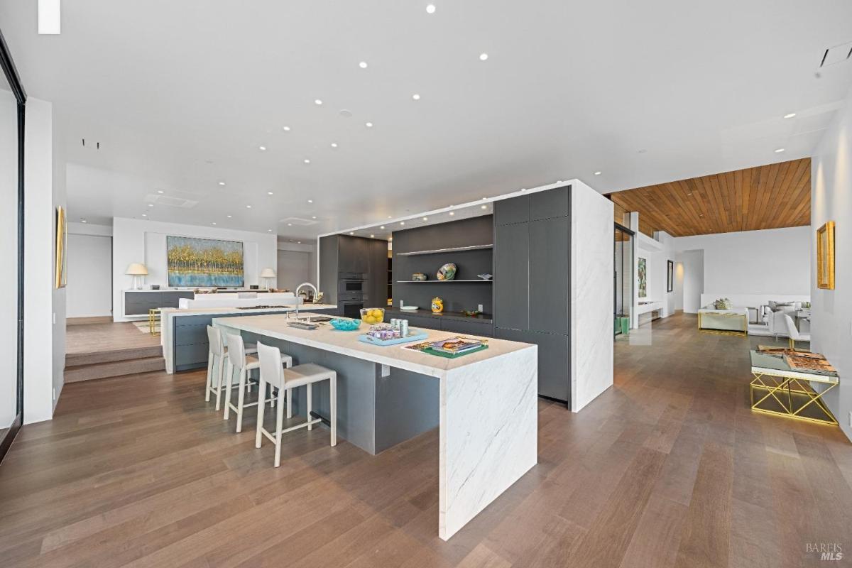 An open-concept kitchen with a large marble island, and a dark cabinetry.