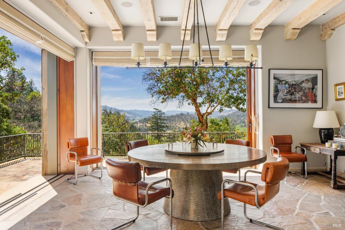 Breakfast nook with a round table, leather chairs, and views through large open doors.