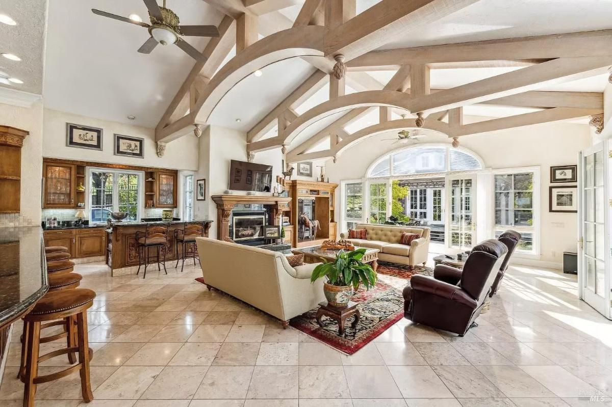 Family room featuring high ceilings with exposed beams, a sitting area with sofas and recliners, a fireplace, and large windows opening to the outside.