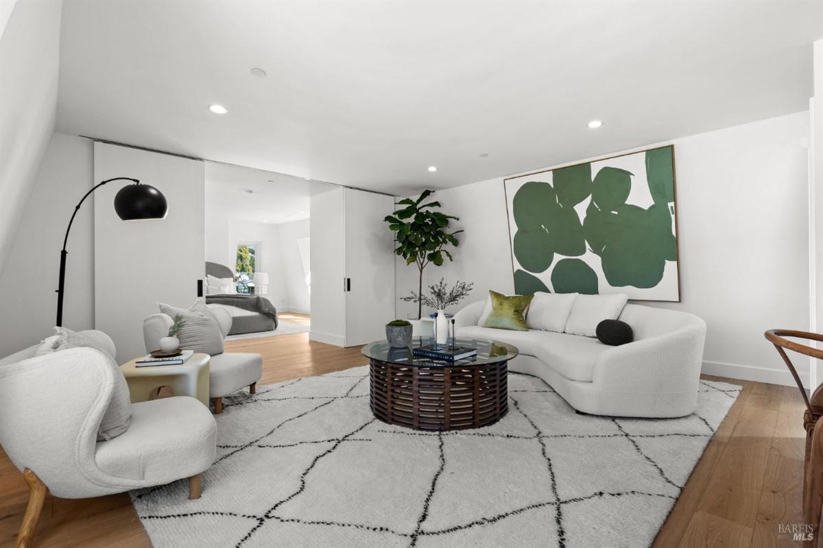 A sitting room with white furniture, a coffee table, and a green wall painting.