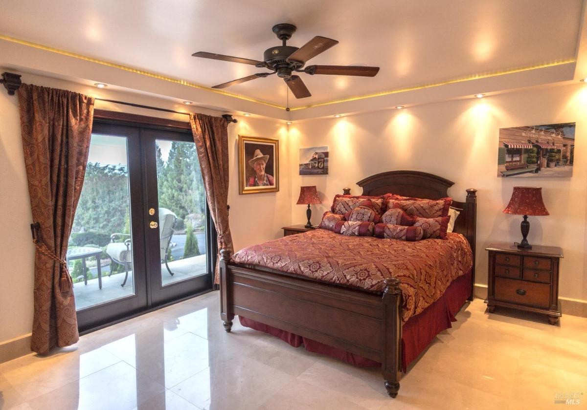 A bedroom featuring a wooden bed with an ornate headboard, decorative bedding, a ceiling fan, and double doors leading to a patio. 