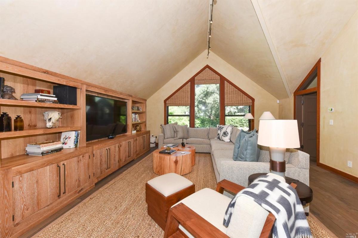 A family room with a sectional sofa, built-in media unit, and large triangular windows.