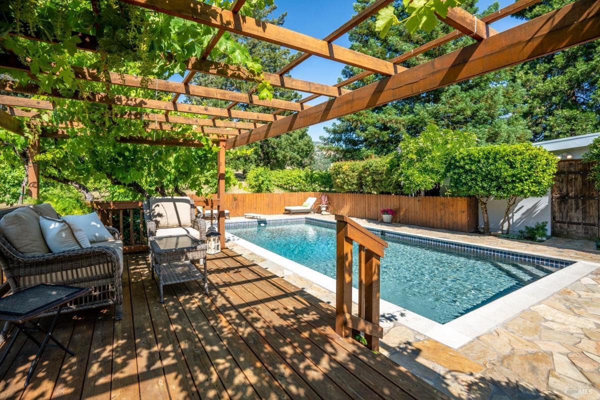 Deck with a pergola overlooking a pool.