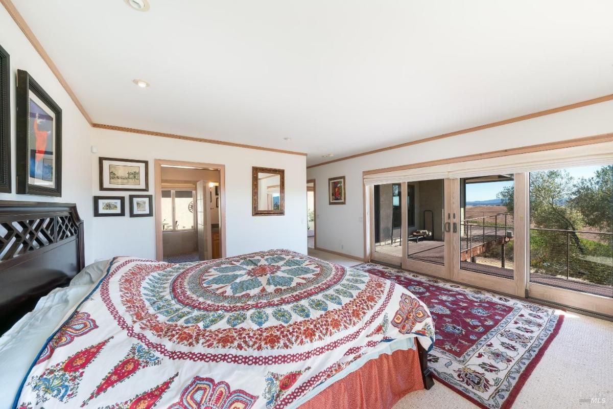 A bedroom with a large window, a patterned bedspread, and sliding doors to a balcony.