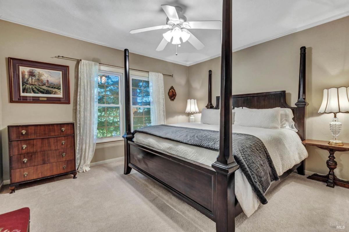 A bedroom with a canopy bed, carpeted floor, and windows framed by curtains.