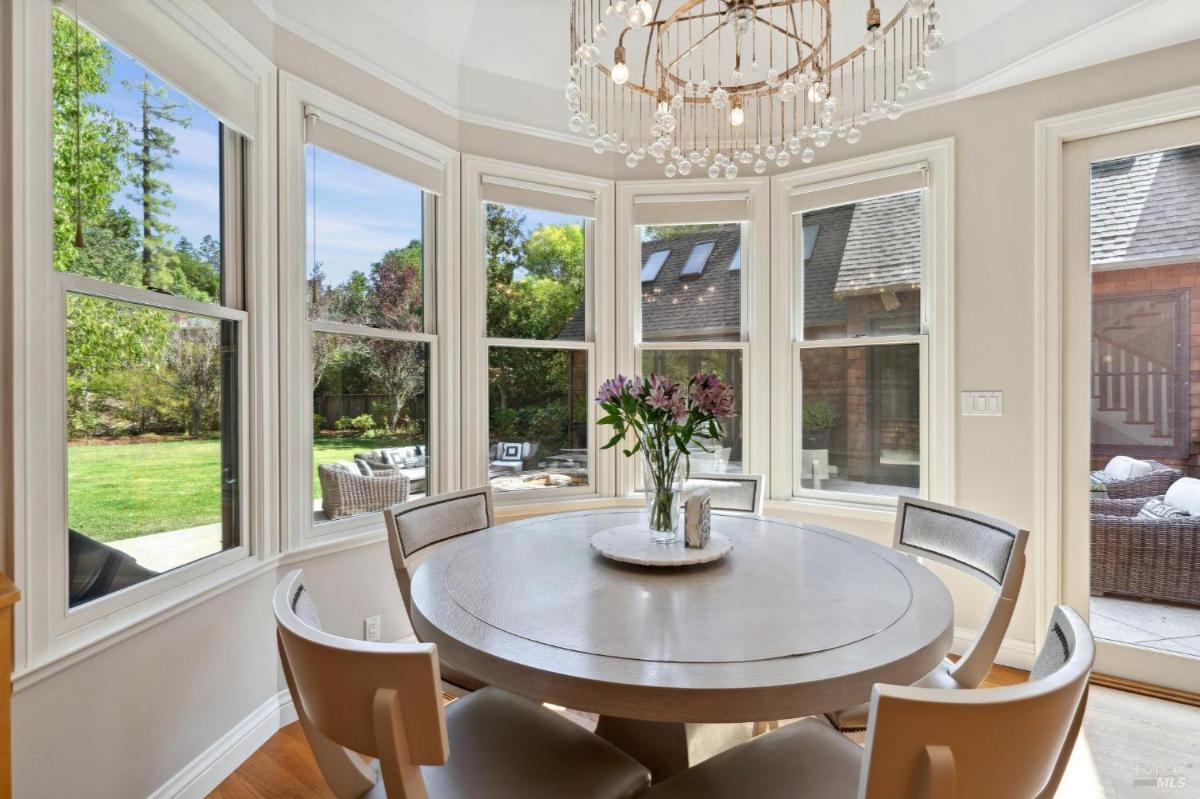 A breakfast nook with a round table, chandelier, and surrounding windows overlooking the backyard.