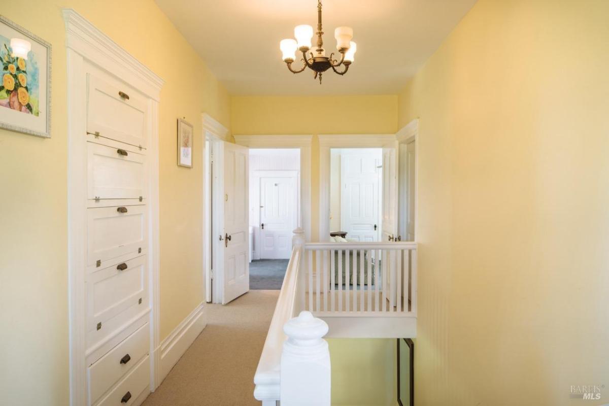 A hallway with yellow walls, built-in storage, and white railings.