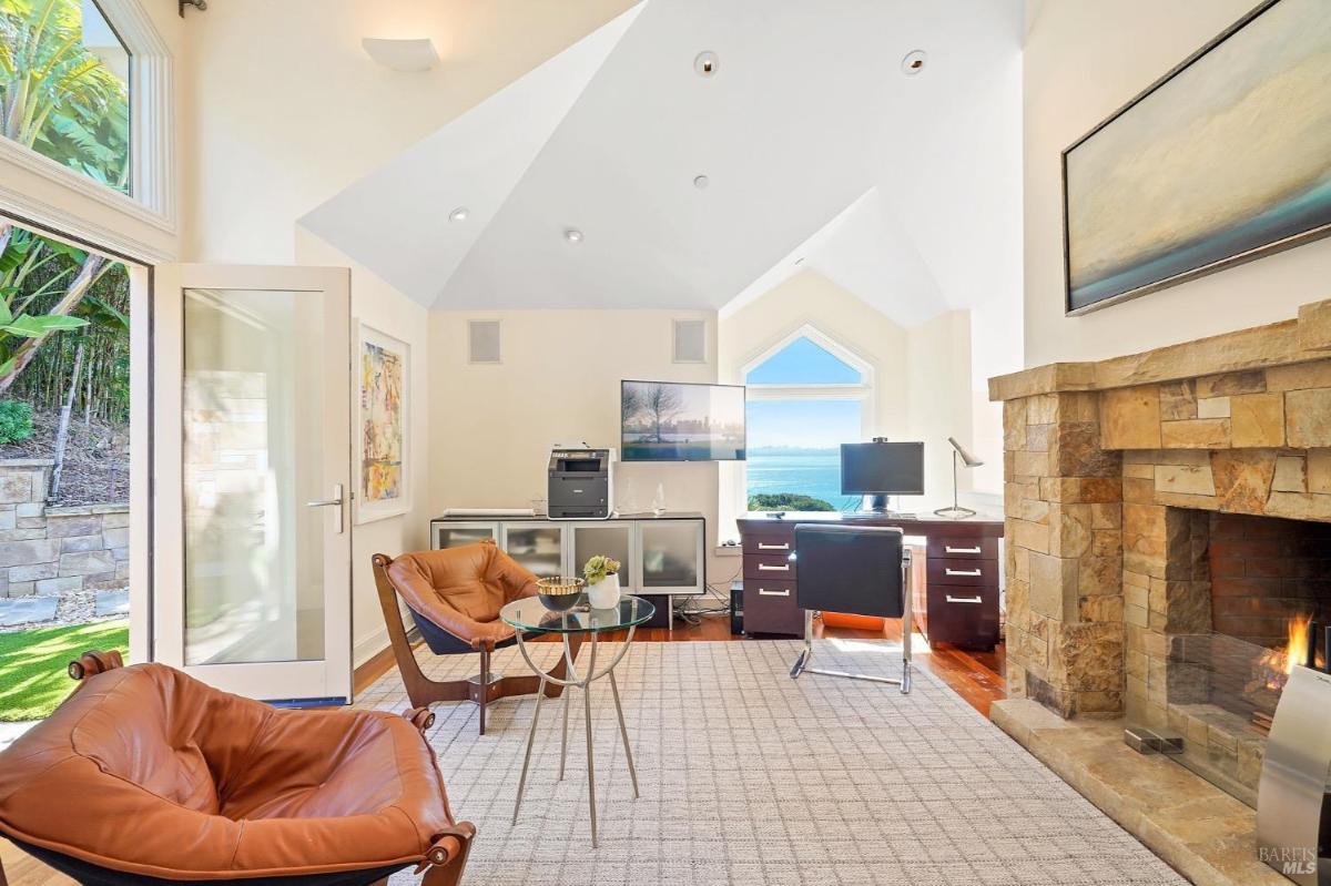 Office room with leather chairs, a stone fireplace, and a desk facing the ocean view.