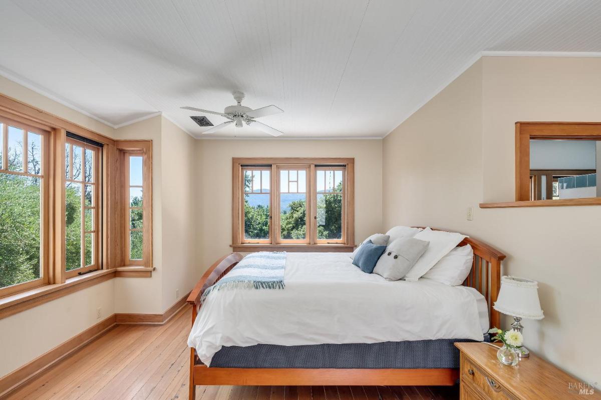 Bedroom with a bed, side table, and windows overlooking trees.