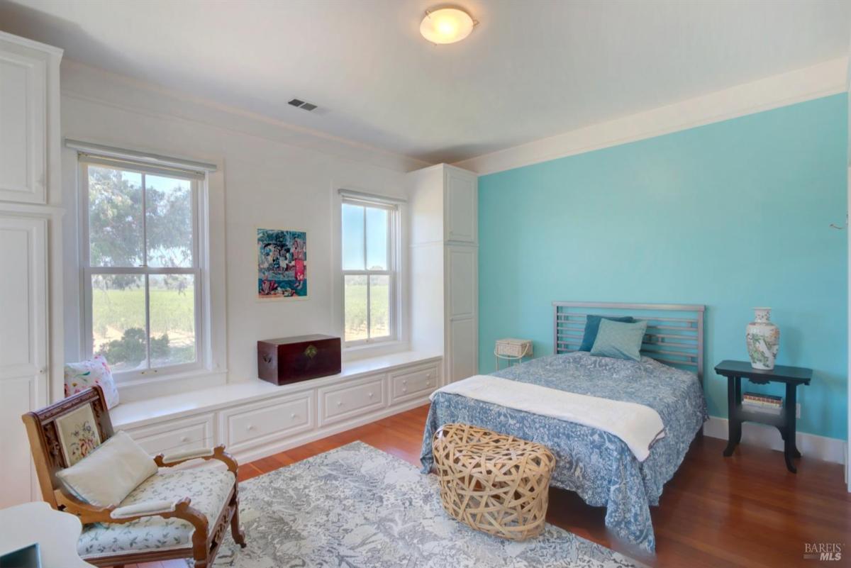 A bedroom with blue walls, a bed, built-in storage under the windows, and a chair in the corner.