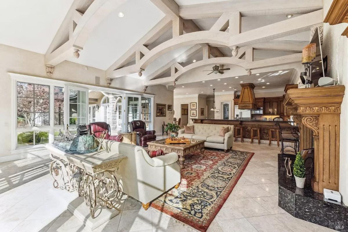 Open concept family room with sofas, a fireplace, large windows, and a connected kitchen with a bar area.